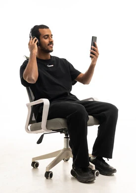 شاب سعودي يرتدي سماعات على كرسي مكتب مع هاتف ذكي