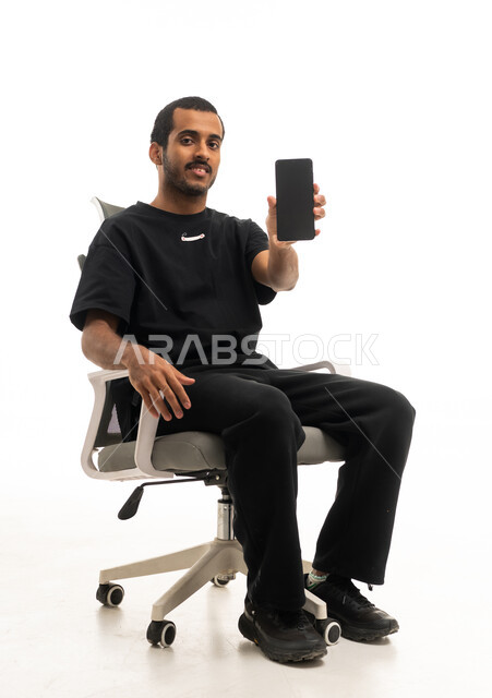 رجل سعودي يحمل هاتف ذكي على كرسي مكتب