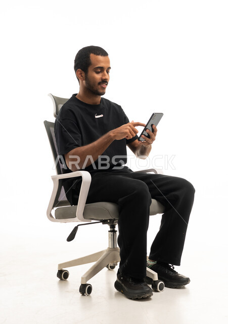 رجل سعودي يستخدم الهاتف الذكي على كرسي مكتب بخلفية بيضاء
