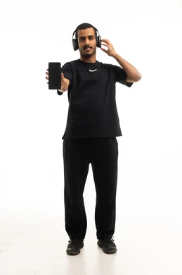 رجل سعودي يحمل هاتفاً ذكياً ويرتدي سماعات رأس