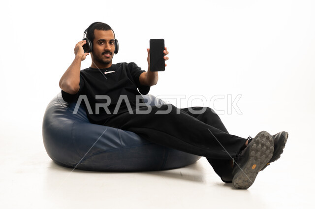 رجل سعودي يحمل هاتفا ذكيا ويرتدي سماعات رأس