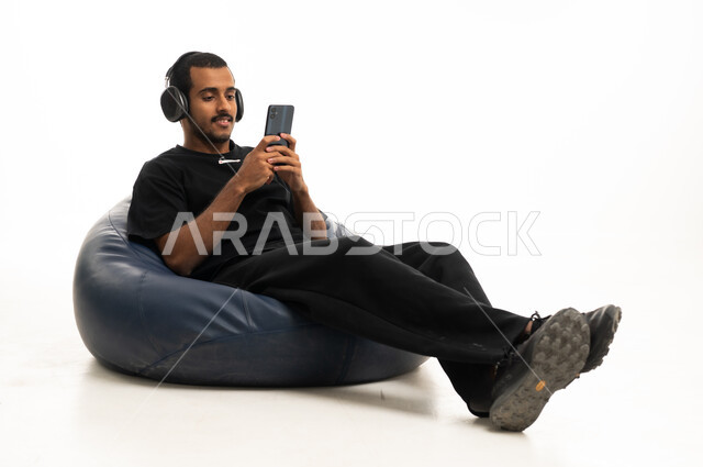 شاب عربي يستخدم الهاتف وسماعات الرأس على مقعد مريح