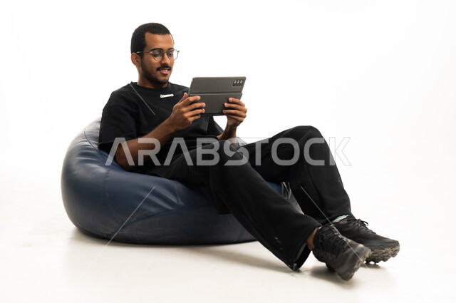 شاب عربي يستخدم جهاز لوحي على مقعد استرخاء خلفية بيضاء