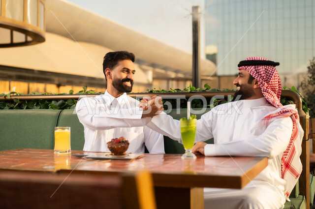 رجلان عربيان يتصافحان في مطعم خارجي وقت الغروب
