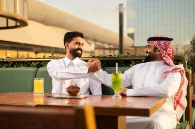 رجلان عربيان يتصافحان في مطعم خارجي وقت الغروب