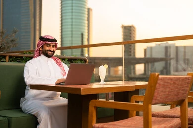 رجل سعودي يستخدم اللابتوب في شرفة مطلة على المدينة