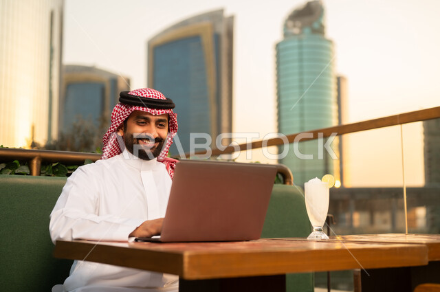 رجل سعودي يعمل على حاسوب محمول في شرفة خارجية