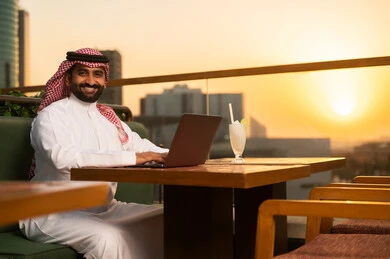رجل سعودي يستخدم اللابتوب في شرفة وقت الغروب
