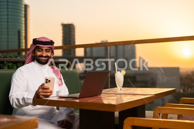 رجل أعمال سعودي مع كمبيوتر وهاتف وقت الغروب