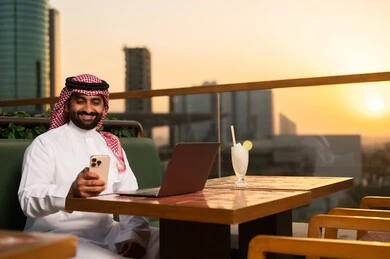 رجل أعمال سعودي مع كمبيوتر وهاتف وقت الغروب