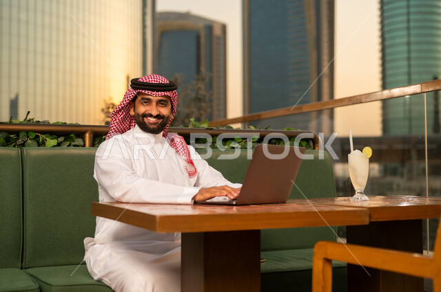 رجل سعودي يعمل على المحمول في مقهى خارجي مع أفق المدينة