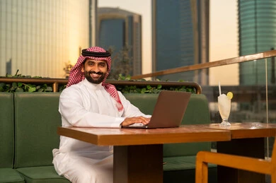 رجل سعودي يعمل على المحمول في مقهى خارجي مع أفق المدينة