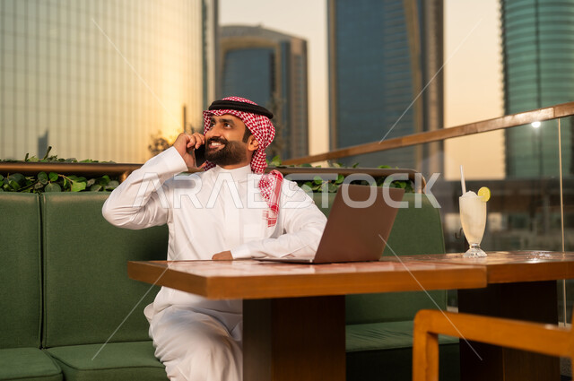 رجل أعمال سعودي يتحدث بالهاتف مع لاب توب وقت الغروب