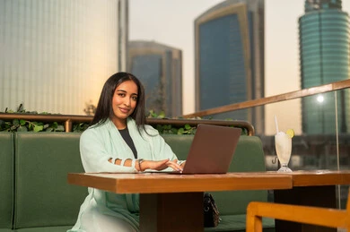 امرأة عربية تعمل على المحمول فوق سطح بمباني حديثة
