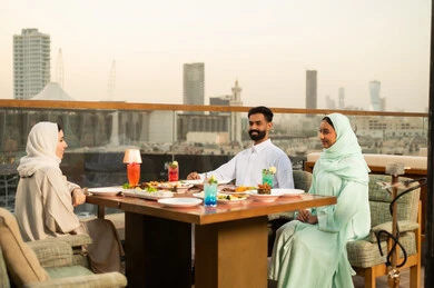 أصدقاء عرب يتناولون العشاء في مطعم خارجي وقت الغروب