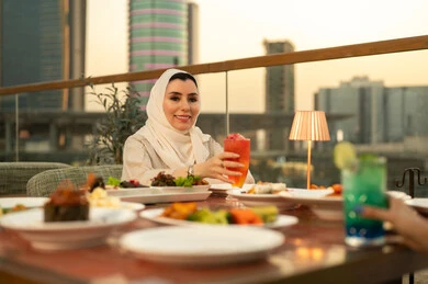 امرأة عربية تتناول الطعام في مطعم على السطح وقت الغروب