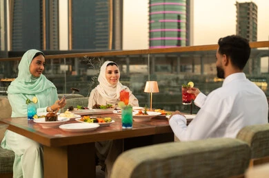 أصدقاء عرب يتناولون الطعام في مطعم بإطلالة غروب