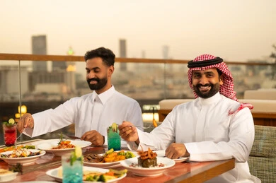 رجال سعوديون يتناولون الطعام في مطعم خارجي وقت الغروب
