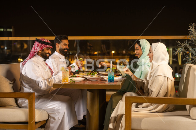 أصدقاء سعوديون يتناولون العشاء في مطعم خارجي ليلاً