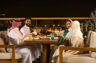 أصدقاء سعوديون يتناولون العشاء في مطعم خارجي ليلاً