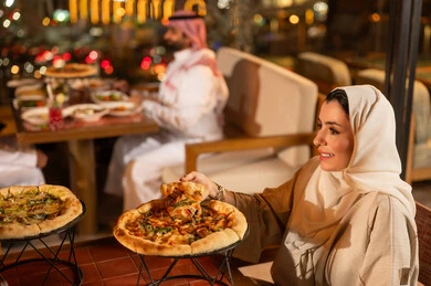 امرأة سعودية تأكل البيتزا في مطعم خارجي ليلاً