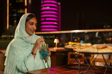امرأة سعودية في مطعم على سطح مدينة ليلاً