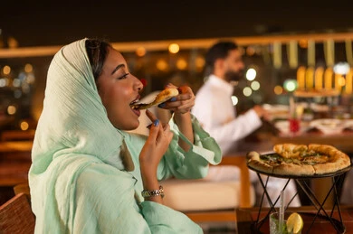 امرأة سعودية تتناول البيتزا في مطعم خارجي ليلاً