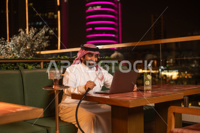 رجل أعمال سعودي يستخدم المحمول مع الشيشة في جلسة ليلية