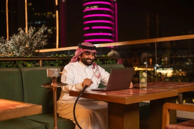 Saudi Businessman Using Laptop and Shisha at Night Lounge