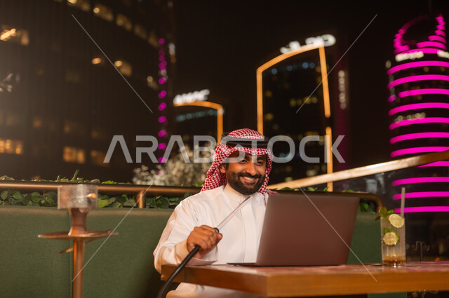 رجل سعودي يستخدم كمبيوتر محمول ويدخن الشيشة ليلاً