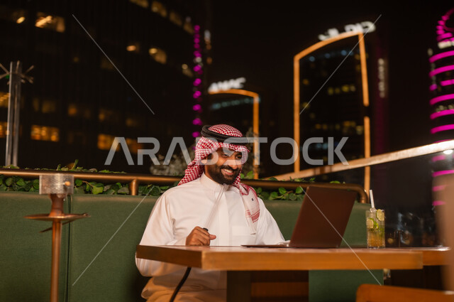 رجل سعودي يعمل على الكمبيوتر في مقهى ليلي