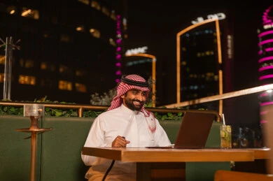 رجل سعودي يعمل على الكمبيوتر في مقهى ليلي