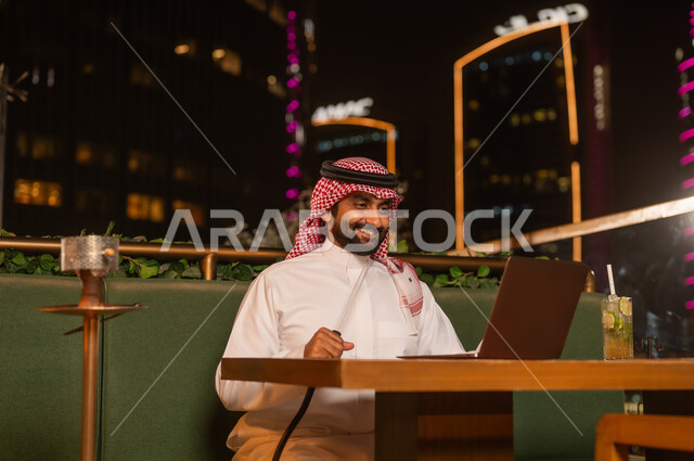 رجل سعودي يستخدم اللابتوب في مقهى ليلي