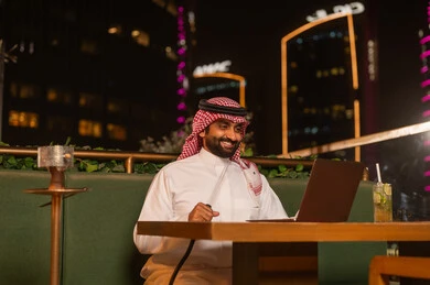 رجل سعودي يستخدم اللابتوب في مقهى ليلي