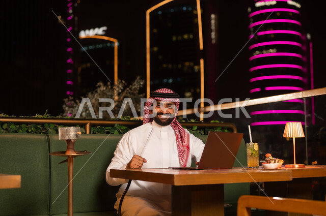 رجل سعودي يستخدم المحمول في مطعم خارجي ليلاً