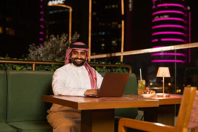 رجل أعمال سعودي يعمل على المحمول في مطعم ليلي