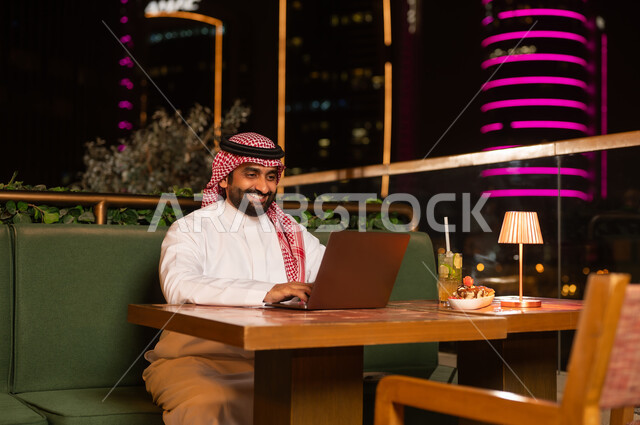 رجل سعودي يعمل على المحمول في مطعم خارجي ليلاً