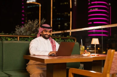 رجل سعودي يعمل على المحمول في مطعم خارجي ليلاً