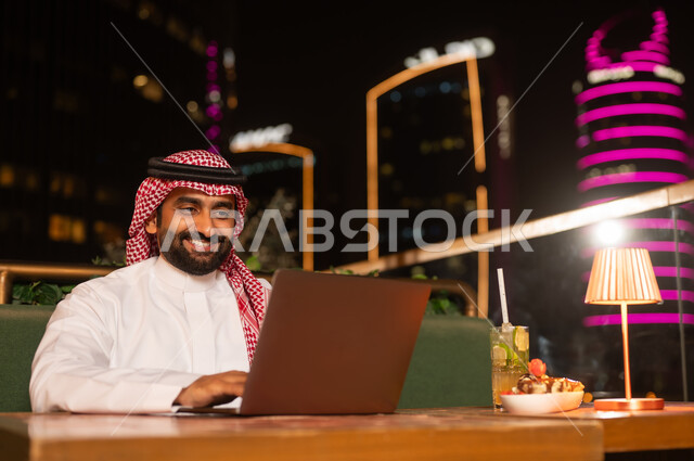 Saudi Man Using Laptop at Night Rooftop Lounge