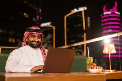 Saudi Man Using Laptop at Night Rooftop Lounge