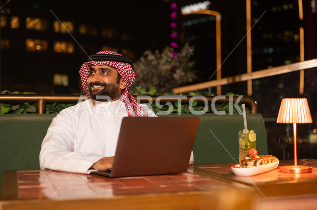 رجل سعودي يستخدم المحمول في مطعم خارجي ليلاً