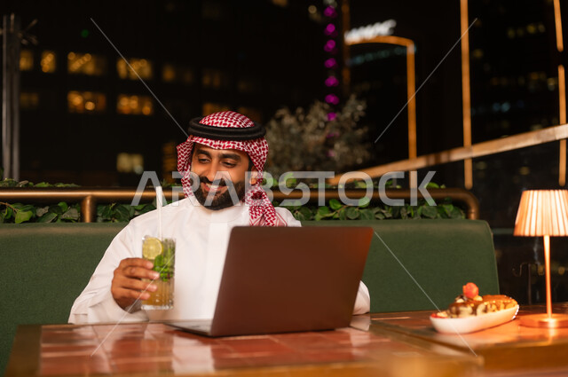 رجل سعودي يعمل على اللابتوب في مطعم خارجي ليلاً