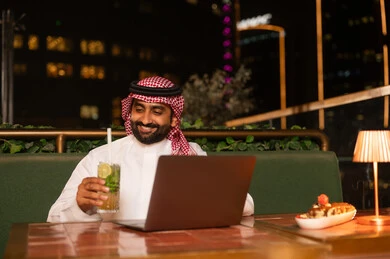 رجل سعودي يعمل على اللابتوب في مطعم خارجي ليلاً