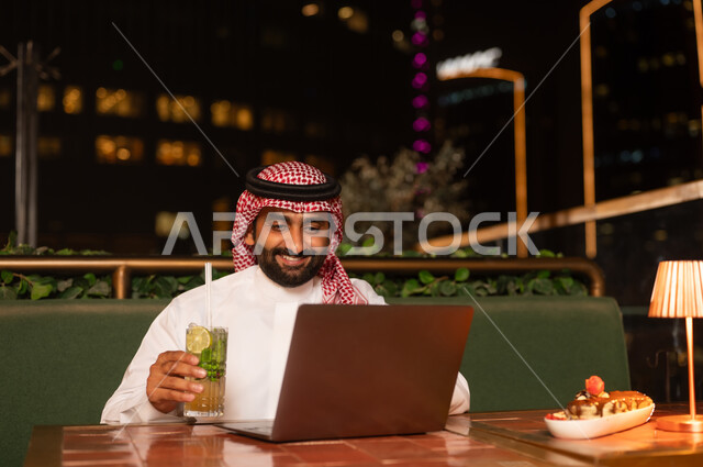 رجل سعودي يستخدم المحمول في مطعم خارجي ليلاً