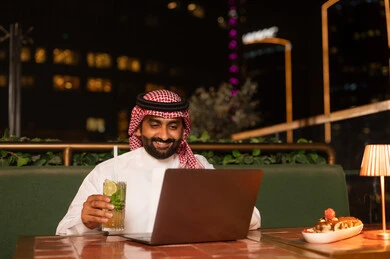 رجل سعودي يستخدم المحمول في مطعم خارجي ليلاً