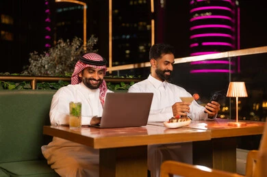 Saudi Men Using Laptop at Night Rooftop Restaurant