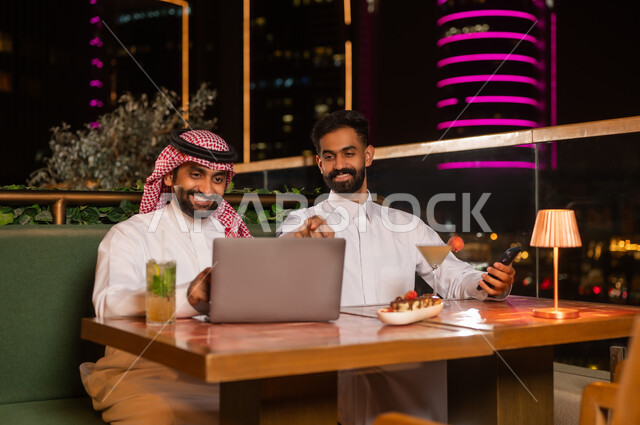 Saudi Men Using Laptop at Night Rooftop Restaurant