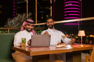 Saudi Men Using Laptop at Night Rooftop Restaurant