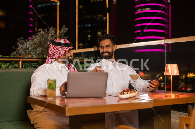 رجال أعمال سعوديون مع كمبيوتر محمول في مطعم ليلي
