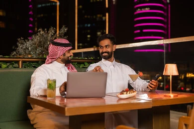رجال أعمال سعوديون مع كمبيوتر محمول في مطعم ليلي